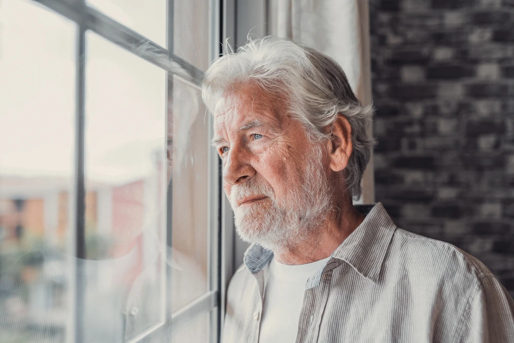 Depressiver Mann im hohen Alter schaut aus dem Fenster